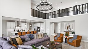Ein großzügiger Wohnbereich mit einer großen Couch, zwei Sesseln und einem Couchtisch. Eine Chandelier hängt von der Decke, und eine Treppe mit Geländer führt zu einer oberen Ebene.