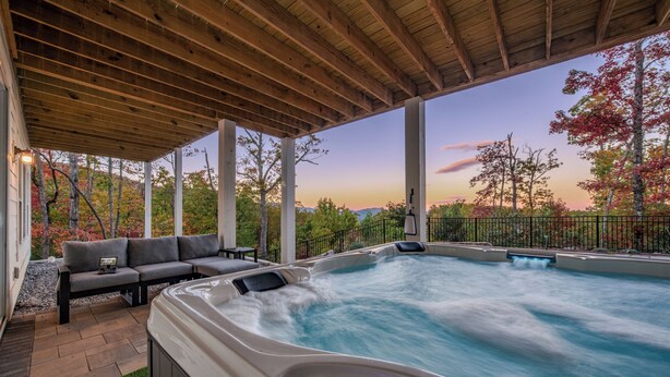 Ein Whirlpool mit Holzterrasse und Sitzgelegenheit im Freien, umgeben von Bäumen und Blick auf die Landschaft.