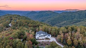 Ein großes, weißes, zweistöckiges Haus mit breiter Veranda, umgeben von dichtem Wald und Bergen im Hintergrund.