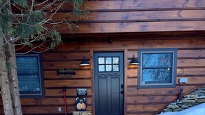 Une cabane en bois avec une porte sombre, une pancarte d’accueil et une pancarte d’avertissement.