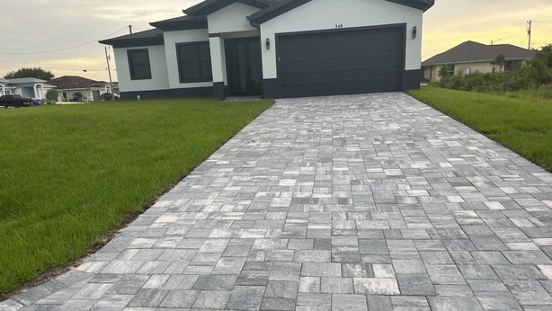 Ein gepflasterter Weg führt zu einem modernen Haus mit Garage, umgeben von gepflegtem Rasen.