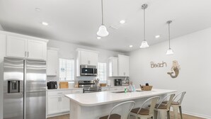 A modern kitchen with white cabinetry, stainless steel appliances, and a central island with bar stools. - Gulfview Paradise in Lost Key (Pensacola)
