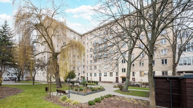 Une cour avec un banc, des arbres et un bâtiment doté de nombreuses fenêtres.