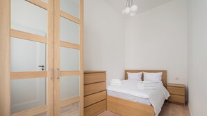 A bedroom with a wooden wardrobe, a bed with white bedding, and a bedside table.