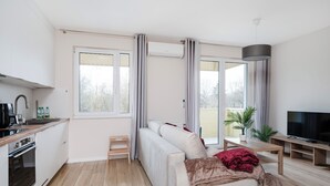 Ein modernes Wohnzimmer mit Sofa, Fernseher, kleinem Tisch und Küchenzeile mit Kaffeemaschine.