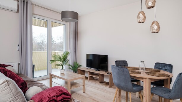 Ein modernes Wohnzimmer mit einer Couch, einem Esstisch mit Stühlen, einem Fernseher und einem Balkon mit Blick.