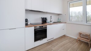 Eine moderne Küche mit weißen Schränken, einer Holz Arbeitsplatte, einem Einbauofen und einem Fenster mit Blick auf Bäume.