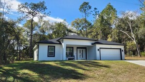 A single-story house with a white exterior and dark roof, a front porch, and a garage. - Beautiful New Home in Citrus Springs, sleep 6 (Citrus Springs)