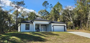 A single-story house with a white exterior and dark roof, a front porch, and a garage. - Beautiful New Home in Citrus Springs, sleep 6 (Citrus Springs)