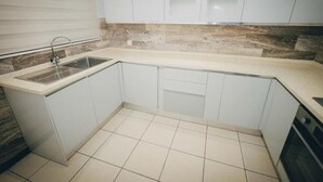 A kitchen with white cabinets, a stainless steel sink, and a tiled backsplash. - Luxury 3BR Alema Court-Airport Close (Accra)