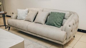 A beige sofa with four cushions in a room with tiled flooring and a small round table. - Luxury 3BR Alema Court-Airport Close (Accra)