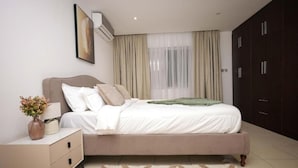 A bedroom with a bed, nightstand, dresser, and a window with curtains. - Luxury 3BR Alema Court-Airport Close (Accra)