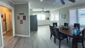 A dining area with a wooden table and chairs, a ceiling fan, and a kitchen in the background.