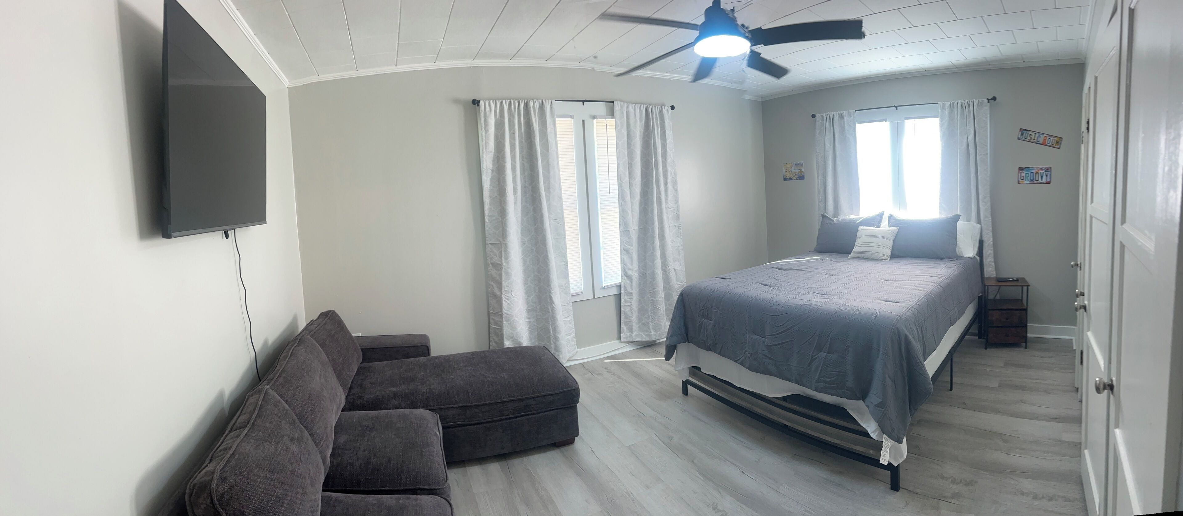Ein Schlafzimmer mit Bett, Sofa, Deckenventilator und Wand-Fernseher.