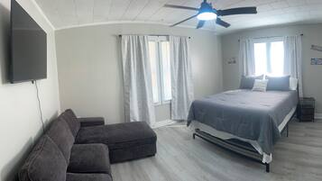 Ein Schlafzimmer mit Bett, Sofa, Deckenventilator und Wand-Fernseher.