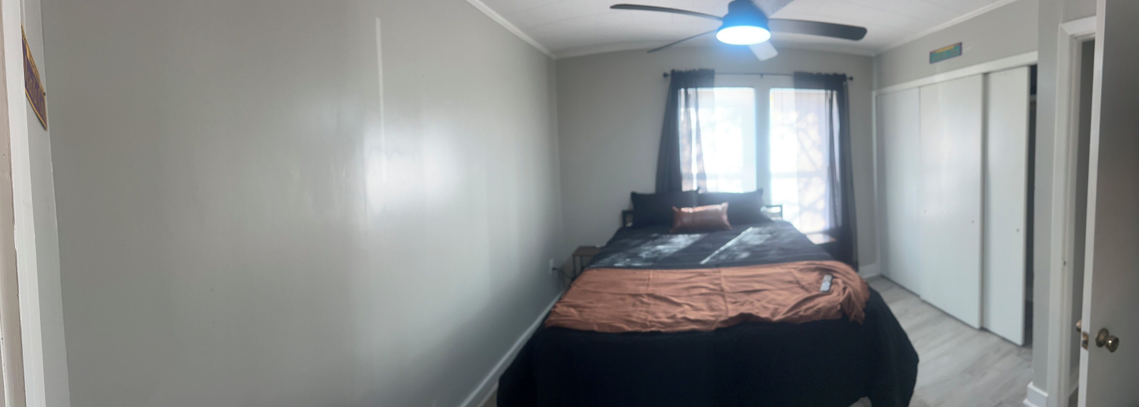 A bedroom with a bed, a ceiling fan, and a window with curtains.