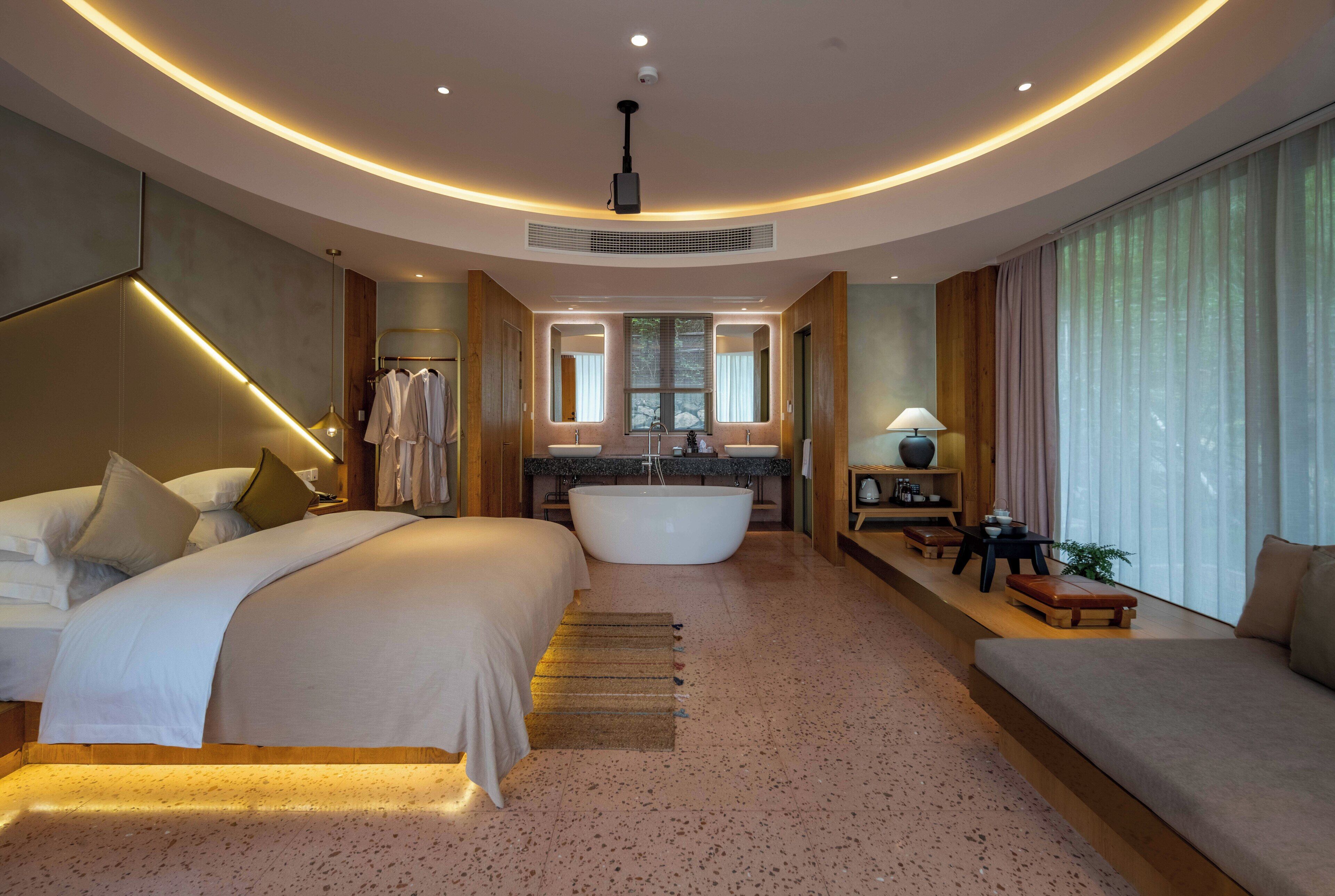 Una habitación de hotel moderna con una cama grande, una bañera, un tocador con espejo y un sofá.