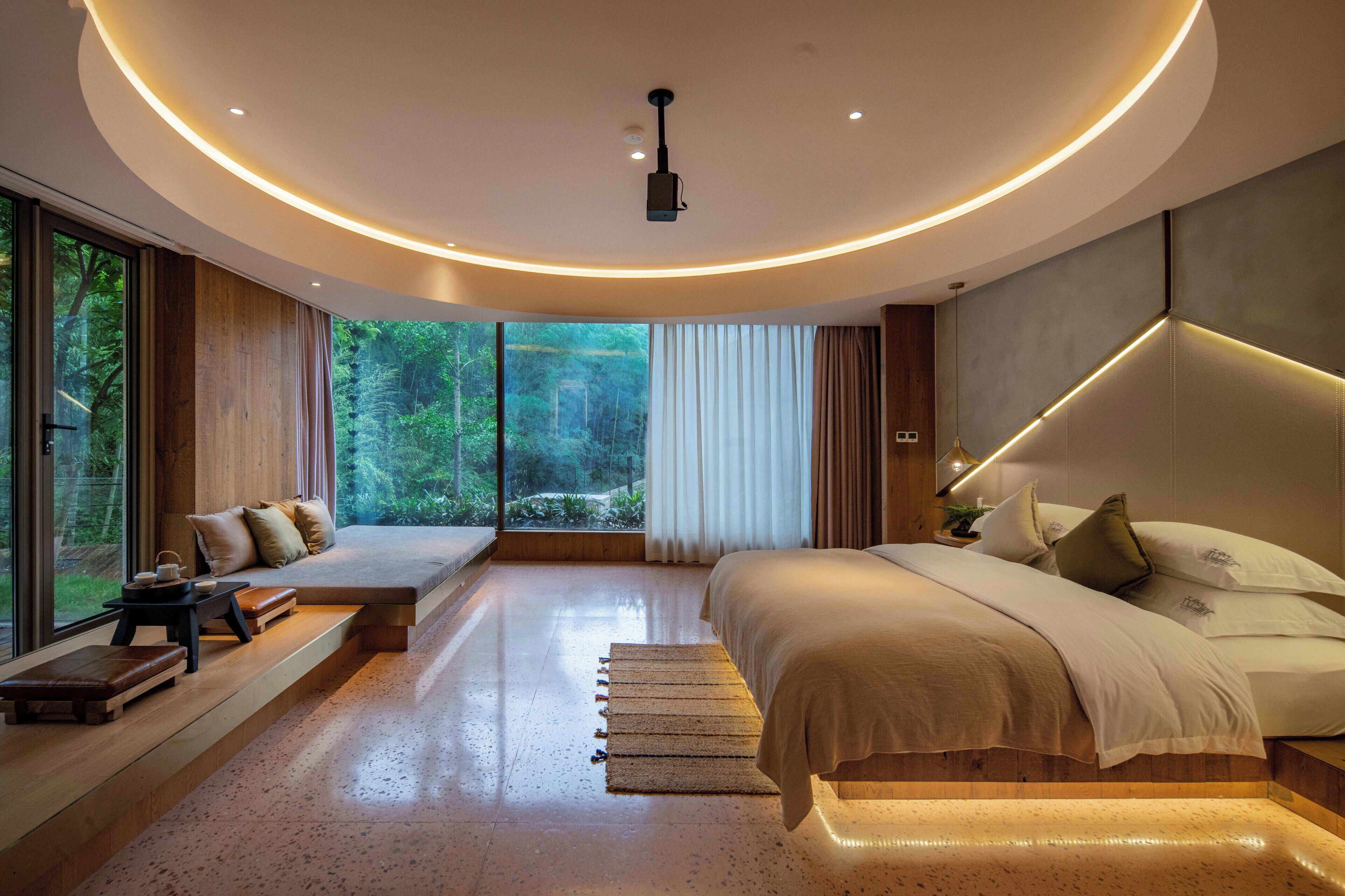 A modern bedroom with a large bed, built-in seating area, and a view of the forest.