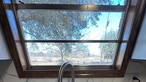 A kitchen with a double sink, a window above the sink, and a view of trees outside. - Lake Life is Calling! Minutes to Cypress Bend Park, private 5-Acre Retreat (Florien)