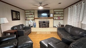 A living room with a fireplace, leather sofas, a ceiling fan, and a TV mounted on the wall. - Lake Life is Calling! Minutes to Cypress Bend Park, private 5-Acre Retreat (Florien)
