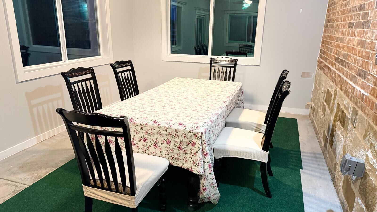 Et spiseområde med et bord dækket af et blomstret dug, omgivet af fire stole, hvoraf den ene er hvid.