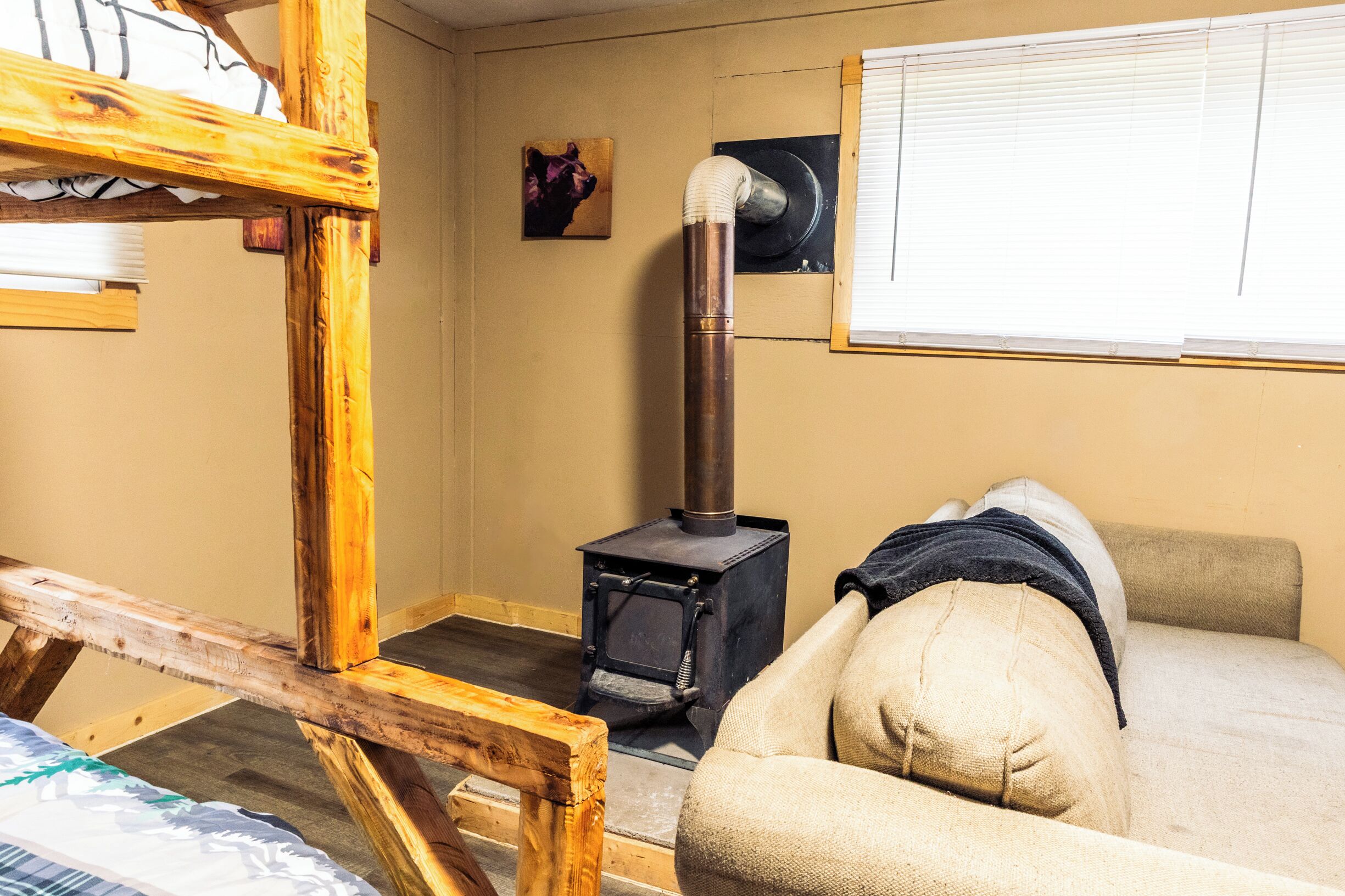 A cozy room with a wooden bed frame, a sofa, a wall-mounted heater, and a window with blinds.