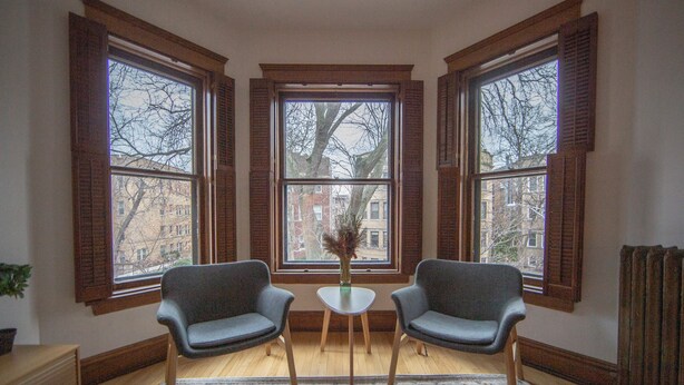 Ein Zimmer mit zwei Stühlen, einem kleinen Tisch und einem großen Fenster mit Rollläden.