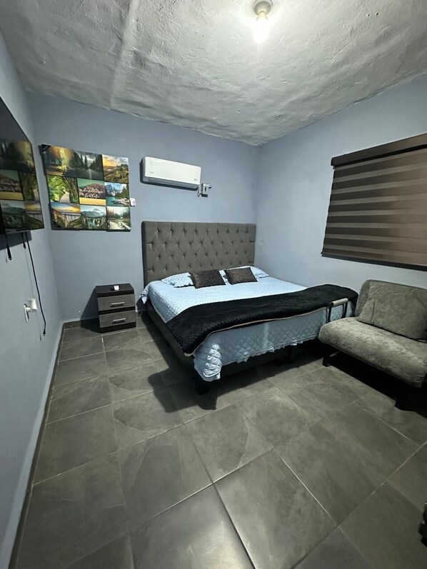 Un dormitorio con cama, sofá, aire acondicionado instalado en la pared y una lámpara en el techo.