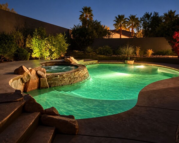 Una piscina con un jacuzzi, rodeada por un muro de piedra y escalones que bajan al agua.