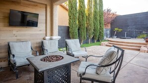 Eine Terrasse mit Sitzgelegenheit im Freien, einem wandmontierten Flachbildfernseher und einem Feuerkorb.
