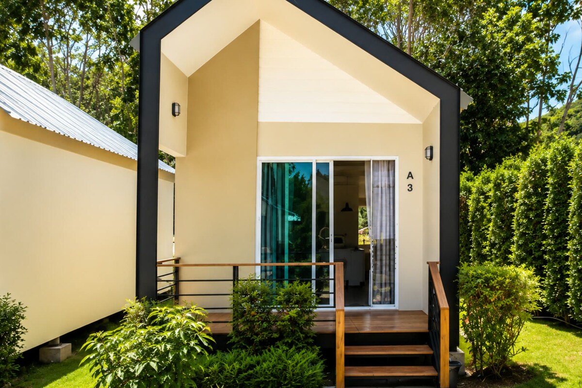 Un bâtiment moderne, de plain-pied, doté d’un toit plat, d’un escalier en bois menant à une entrée avec une porte en verre, et du chiffre « 3 » peint sur le mur.