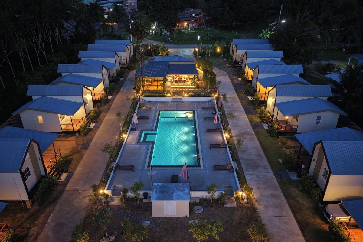 Un resort con varias cabañas tipo bungalow, una piscina central y senderos bien iluminados.