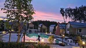 A pool area with lounge chairs and umbrellas, surrounded by trees and buildings. - NaraRin Family House (Thep Krasattri)