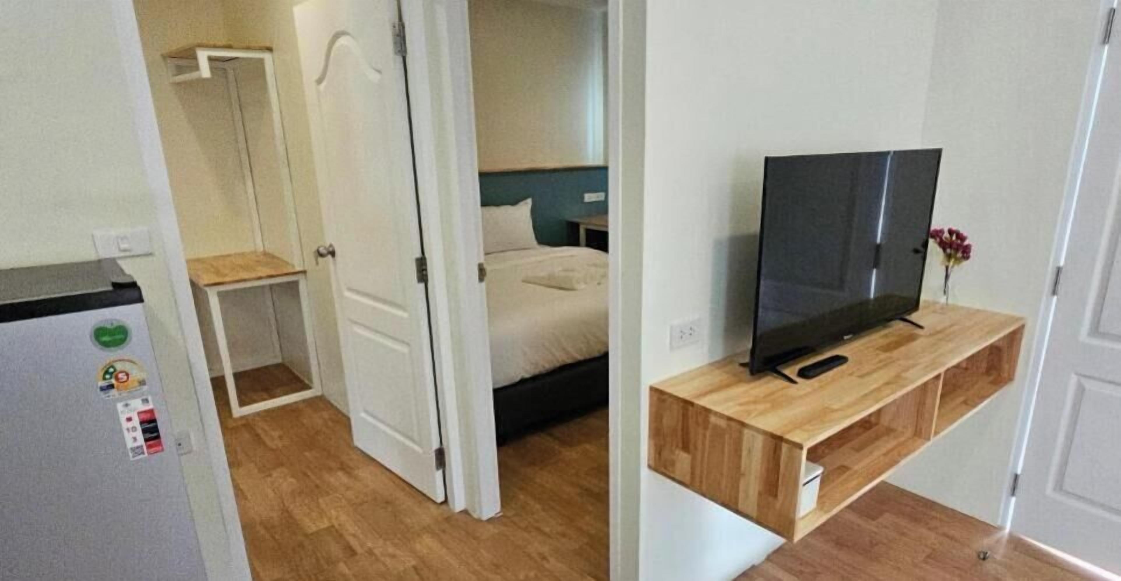A bedroom with a bed, a television on a wooden stand, and a door leading to another room.