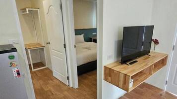 A bedroom with a bed, a television on a wooden stand, and a door leading to another room.