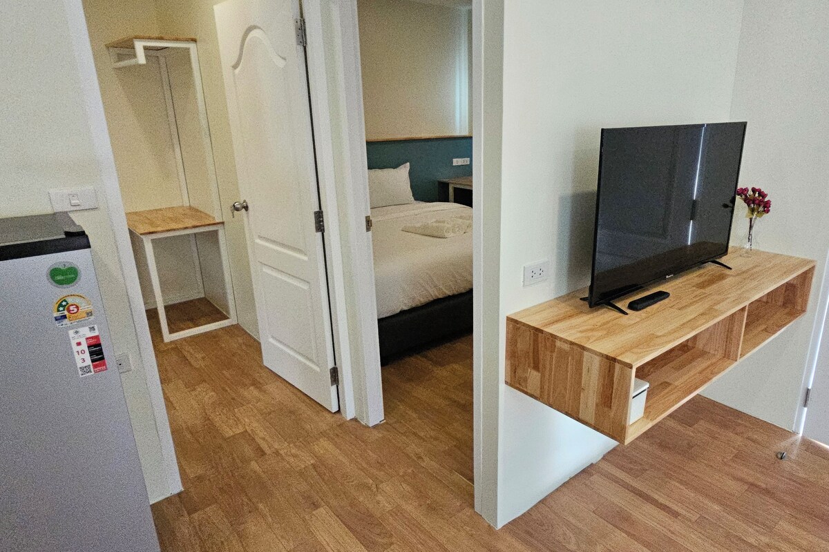 Una habitación pequeña con una cama, un televisor sobre un mueble de madera y un refrigerador.