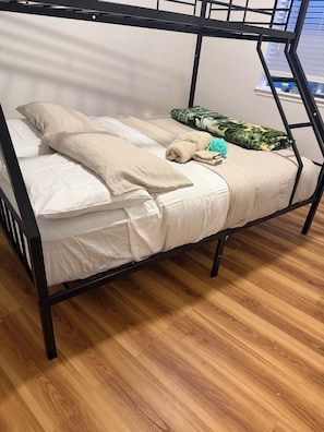 Una cama litera con ropa blanca y una manta verde estampada.