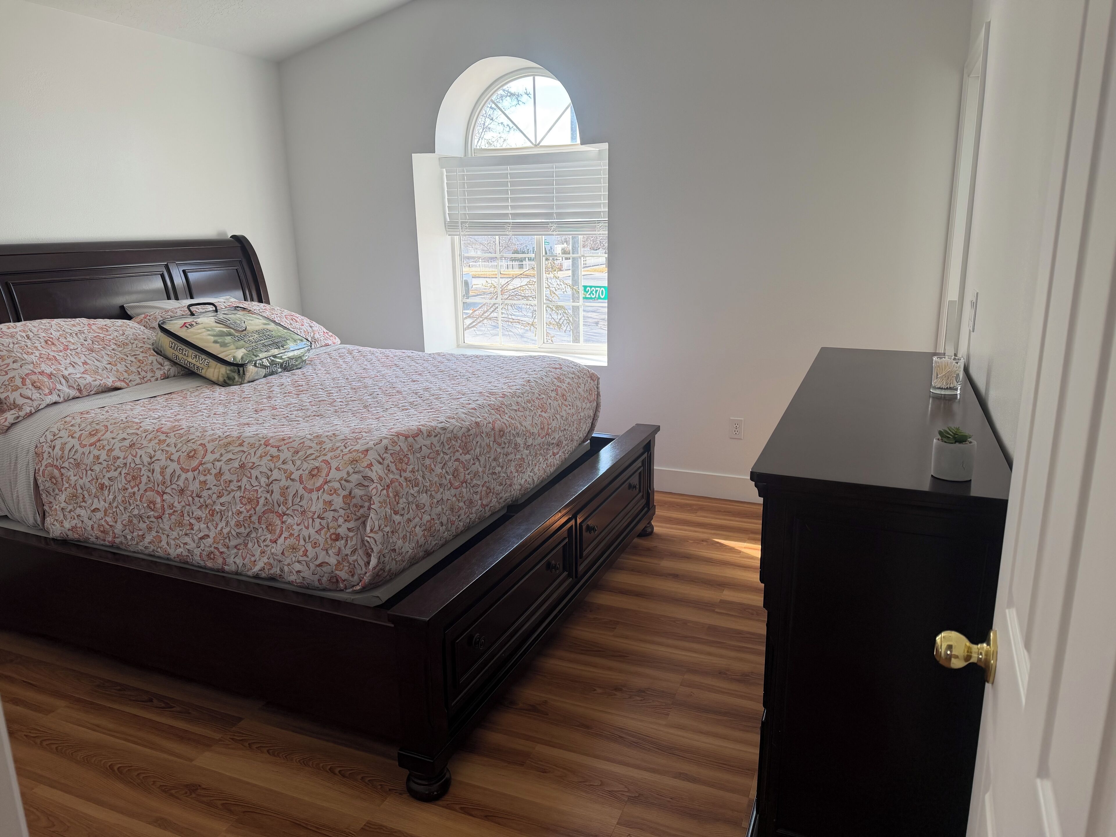 A bedroom with a bed, a dresser, a window, and a door.