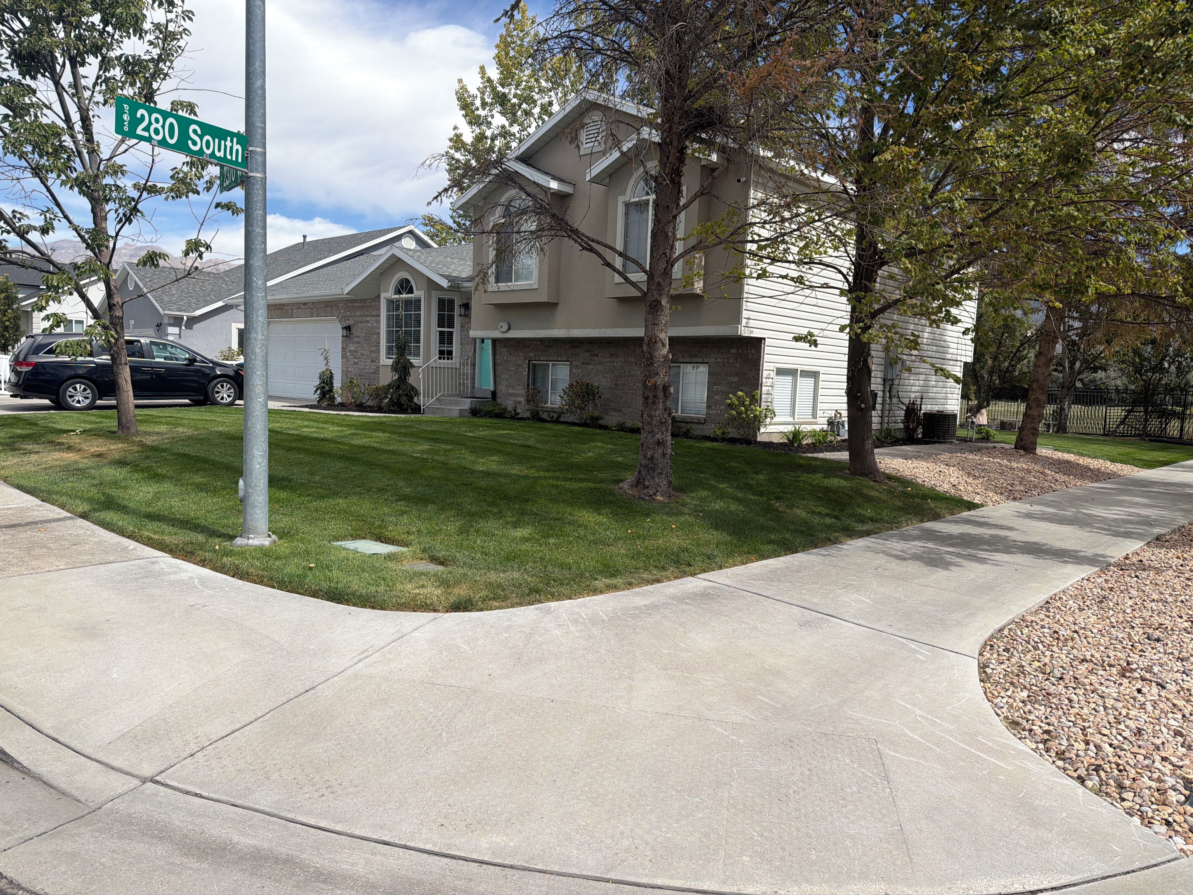 A residential street with a house featuring a front yard, a driveway, and a parked car.