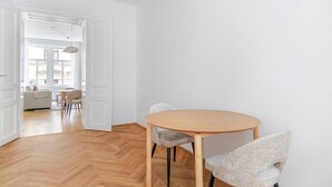 A minimalist room with a round wooden table and two chairs, a white door leading to another room, and a herringbone-patterned wooden floor. - Blueground | Neubau, view, nr Museumsquartier (Vienna)