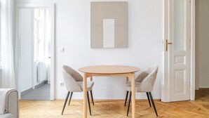 Ein Zimmer mit einem runden Holztisch, zwei grau gepolsterten Sesseln, einer weißen Tür und einem gerahmten abstrakten Kunstwerk an der Wand.