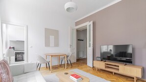 Ein modernes Wohnzimmer mit einer Couch, einem Couchtisch mit Büchern, einem Fernseher und einem Essbereich mit Stühlen.