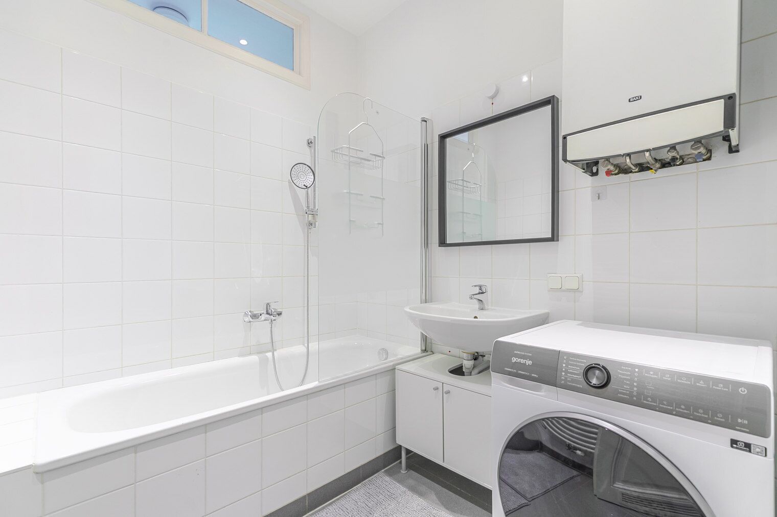 Een moderne badkamer met bad, douche, wastafel en een ingebouwde wasmachine.