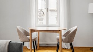 A room with a round wooden table and two chairs, a window with a view of a building, and a radiator. - Blueground | Neubau, view, nr MuseumsQuartier (Vienna)