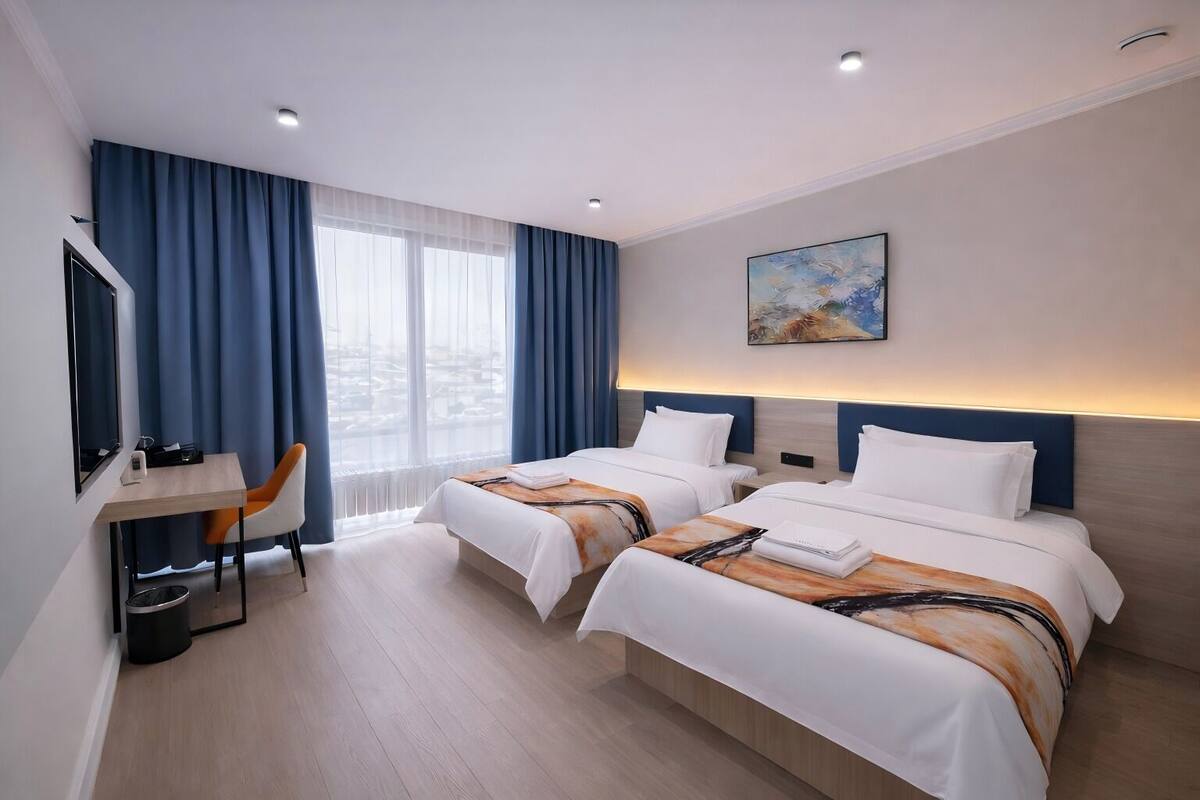 Habitación de hotel con dos camas, un escritorio, una silla, un televisor y un cuadro en la pared.