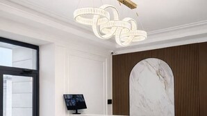 A modern reception area with a marble reception desk, a large marble wall, and a unique ceiling light fixture. - Huaxia Hotel Bishkek (Bishkek)