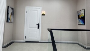 A clean, modern hallway with a white door, numbered room sign, and artwork on the walls. - Huaxia Hotel Bishkek (Bishkek)