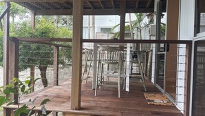 Une terrasse en bois, avec des chaises et une table en métal, entourée d’une clôture en métal et d’arbres.
