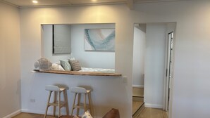 Une cuisine moderne avec un plan de travail en bois, deux tabourets de bar et un tableau abstrait suspendu au mur.