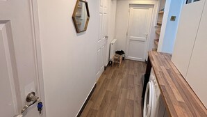 Un couloir étroit avec un plancher en bois, des murs blancs et un lave-linge sur le côté droit.